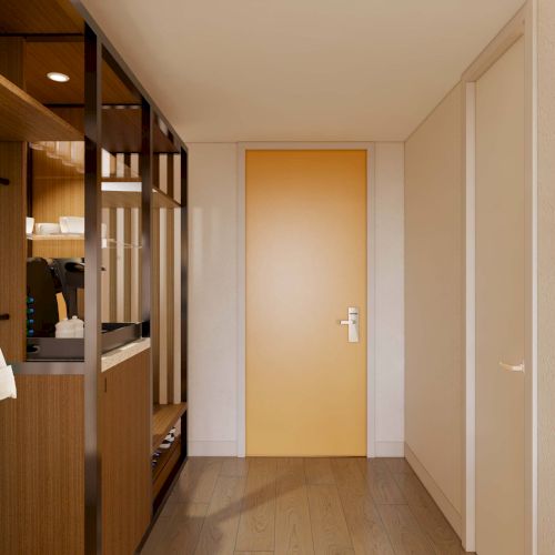 A hallway with wooden flooring, a yellow door, a coat on a rack, shelves with items, and a framed picture on the wall.