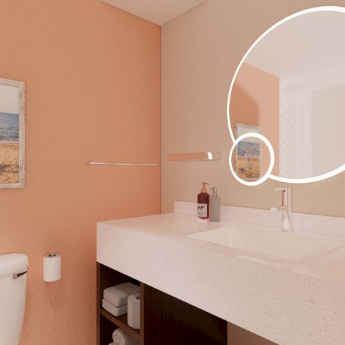 A modern bathroom with a round mirror, sink, peach walls, art on the wall, and a toilet.