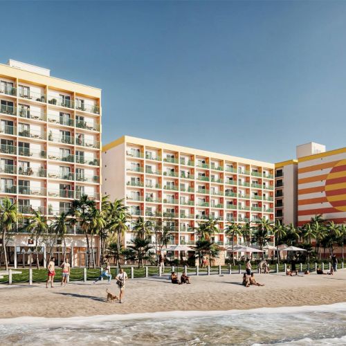 The image shows a beachfront hotel with colorful balconies, palm trees, and people enjoying the sandy beach under a clear sky.