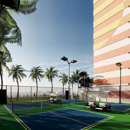 The image shows a tennis court next to a colorful building, surrounded by palm trees under a clear sky.