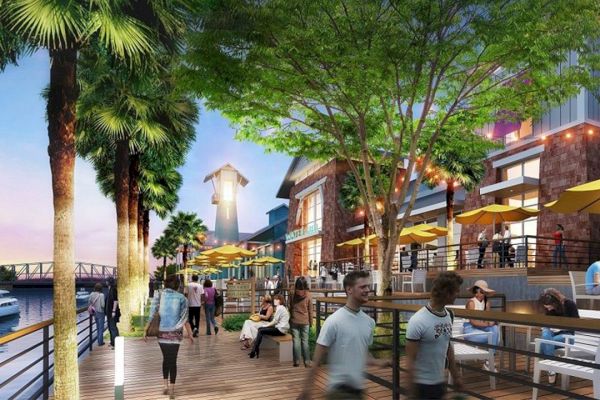 A lively waterfront boardwalk with people, palm trees, outdoor dining under yellow umbrellas, and boats on the water.