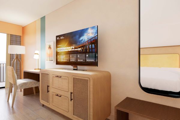 A hotel room with a modern design, featuring a wall-mounted TV, wooden furniture, a desk with a lamp, and a bed partially visible.