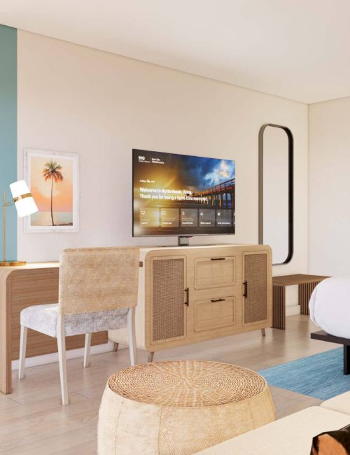 This image shows a modern hotel room with a bed, TV, desk, chair, and decor. The design features soft colors and contemporary furniture.