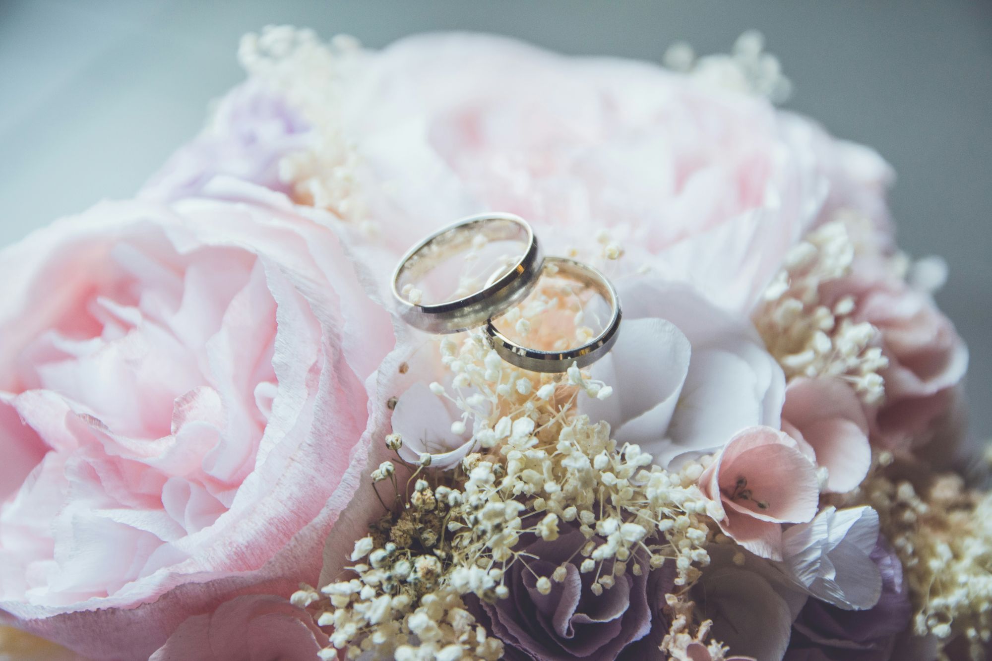 Two wedding rings rest on a bouquet of pink and white flowers, surrounded by delicate baby's breath.