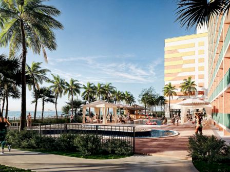 A beachside resort featuring a pool, palm trees, and people relaxing under cabanas; a tall building is in the background.