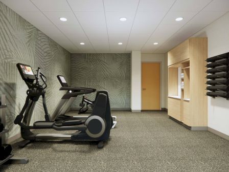 The image shows a gym with treadmills, dumbbells, a patterned wall, fluorescent lighting, and a storage cabinet with additional weights.