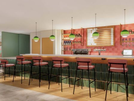 The image shows a modern bar with high chairs, pendant lights, and a well-stocked counter, featuring a stylish and contemporary design.