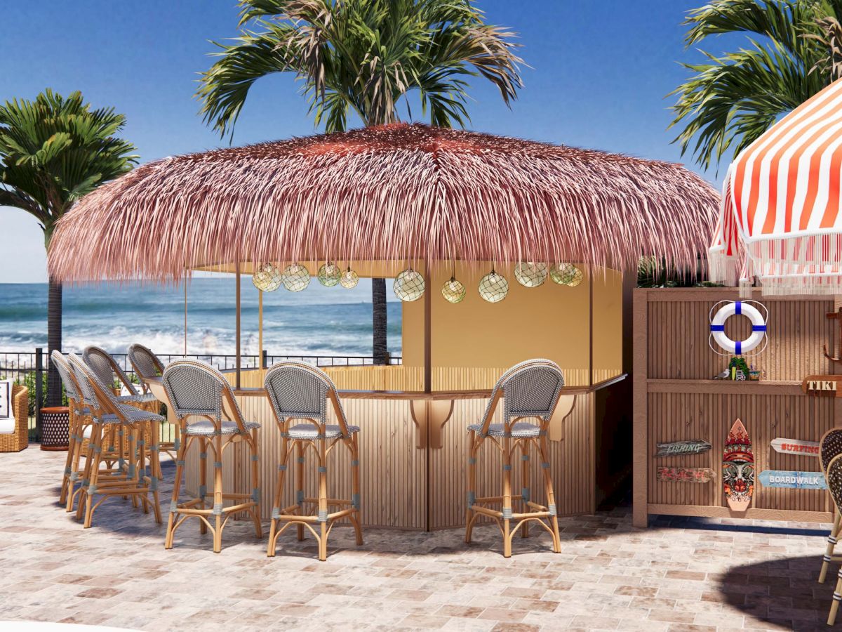 Outdoor tiki bar with wooden stools, palm trees, ocean view, and decorative lights under a thatched roof, creating a tropical vibe.