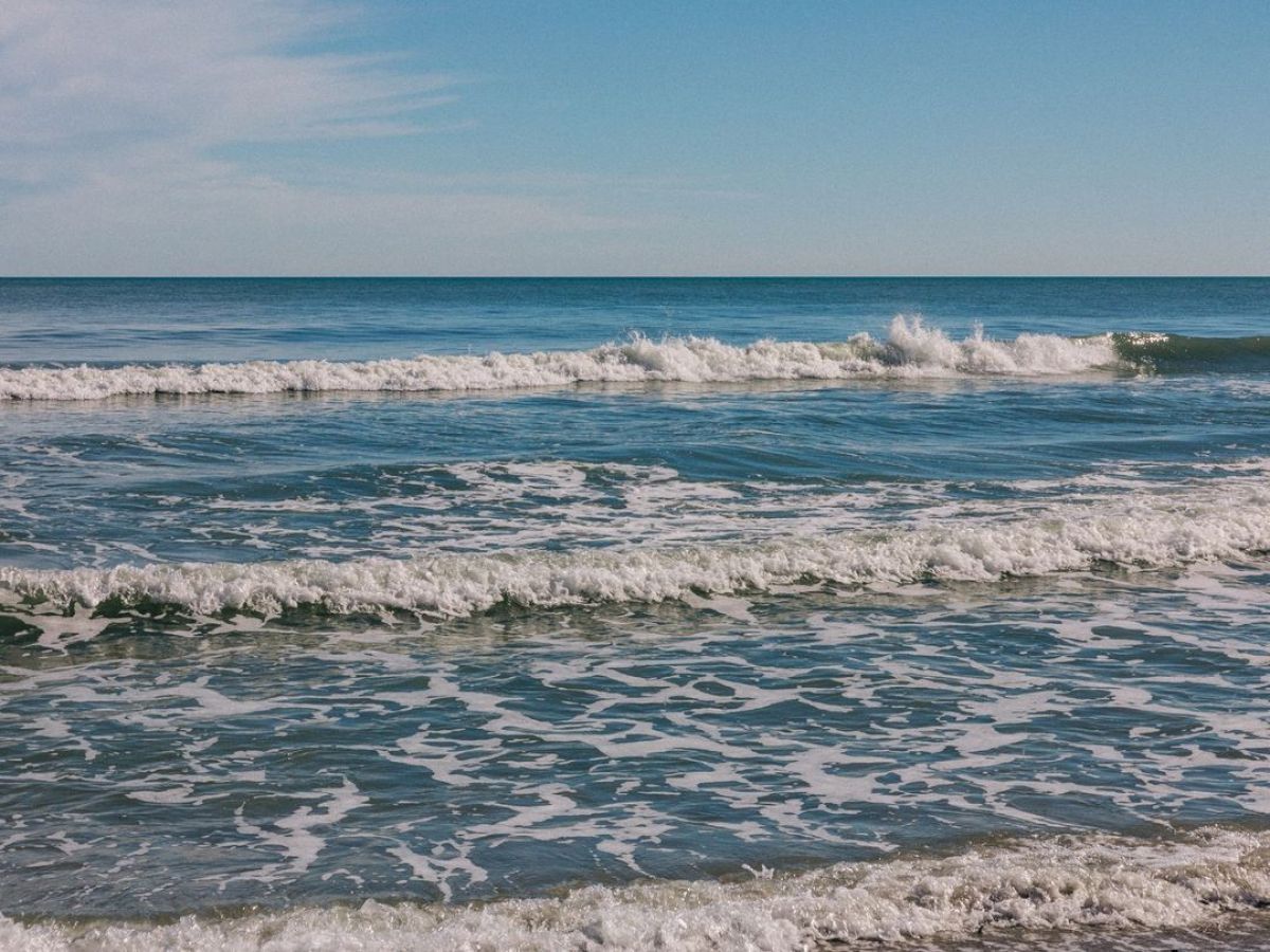 A serene beach scene with waves crashing on the shore under a clear blue sky.